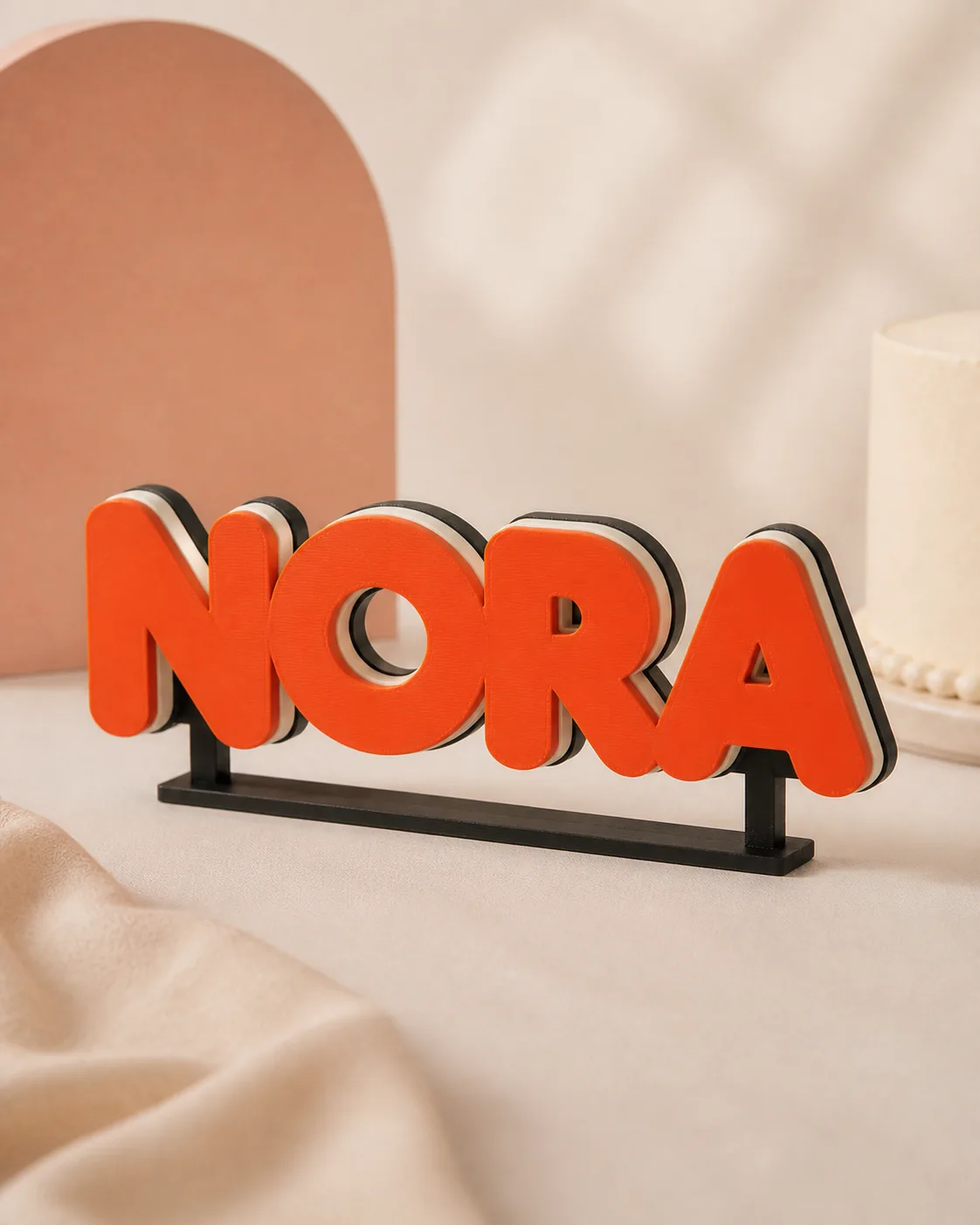 Freestanding layered NORA name sign in orange, cream, and black